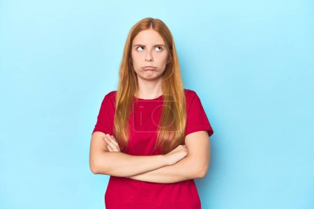Photo for Redhead young woman on blue background tired of a repetitive task. - Royalty Free Image