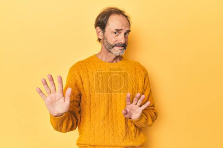 Foto de Caucásico hombre de mediana edad en estudio amarillo rechazando a alguien que muestra un gesto de disgusto. - Imagen libre de derechos