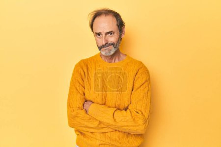 Photo for Caucasian middle-aged man in yellow studio unhappy looking in camera with sarcastic expression. - Royalty Free Image