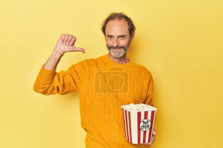 Téléchargez les photos : Homme appréciant le pop-corn en studio jaune se sent fier et confiant, exemple à suivre. - en image libre de droit