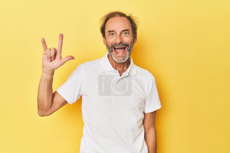 Téléchargez les photos : Homme d'âge moyen caucasien en studio jaune montrant un geste de cornes comme un concept de révolution. - en image libre de droit