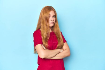 Photo for Redhead young woman on blue background suspicious, uncertain, examining you. - Royalty Free Image