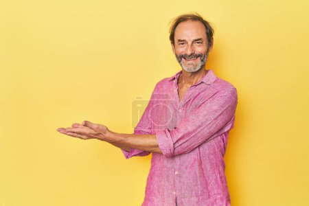 Foto de Caucásico hombre de mediana edad en estudio amarillo sosteniendo un espacio de copia en una palma. - Imagen libre de derechos