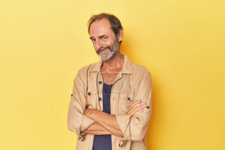 Photo for Caucasian middle-aged man in yellow studio suspicious, uncertain, examining you. - Royalty Free Image