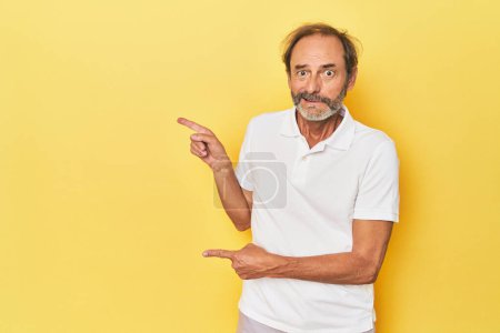 Téléchargez les photos : Blanc d'âge moyen homme en studio jaune choqué pointant avec des index à un espace de copie. - en image libre de droit