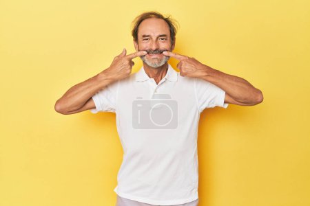 Téléchargez les photos : Blanc d'âge moyen homme en jaune studio sourit, les doigts pointant vers la bouche. - en image libre de droit