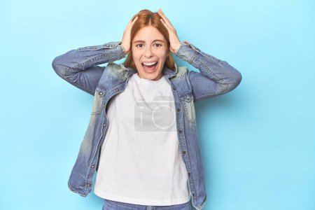 Photo for Redhead young woman on blue background screaming, very excited, passionate, satisfied with something. - Royalty Free Image