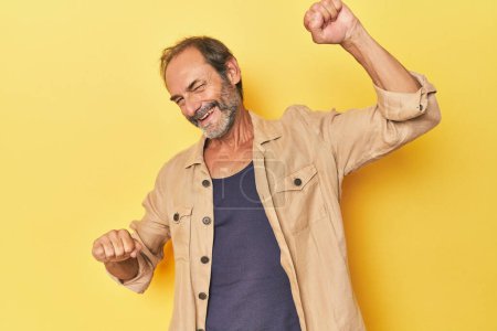 Photo for Caucasian middle-aged man in yellow studio celebrating a special day, jumps and raise arms with energy. - Royalty Free Image
