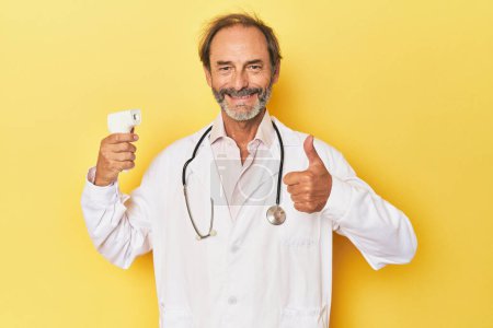 Foto de Doctor sosteniendo termómetro infrarrojo en estudio sonriendo y levantando el pulgar hacia arriba - Imagen libre de derechos