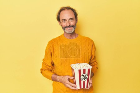 Foto de Hombre disfrutando de palomitas de maíz en estudio amarillo feliz, sonriente y alegre. - Imagen libre de derechos