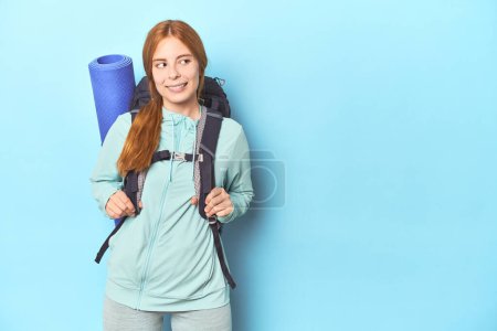 Photo for Mountaineer redhead with backpack and mat on blue background - Royalty Free Image