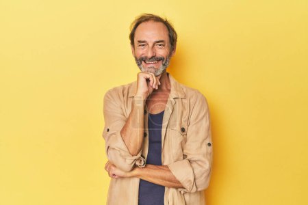 Téléchargez les photos : Blanc homme d'âge moyen en studio jaune souriant heureux et confiant, toucher le menton avec la main. - en image libre de droit