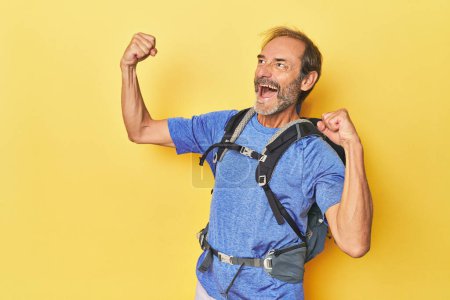 Photo for Middle-aged hiker with backpack in studio raising fist after a victory, winner concept. - Royalty Free Image