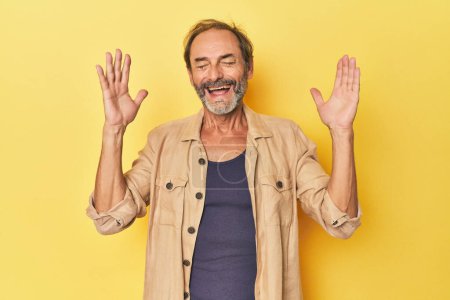 Photo for Caucasian middle-aged man in yellow studio joyful laughing a lot. Happiness concept. - Royalty Free Image