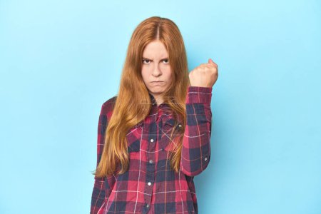 Photo for Redhead young woman on blue background showing fist to camera, aggressive facial expression. - Royalty Free Image