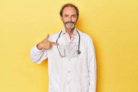 Téléchargez les photos : Docteur avec stéthoscope en studio jaune personne pointant à la main vers un espace de copie chemise, fier et confiant - en image libre de droit