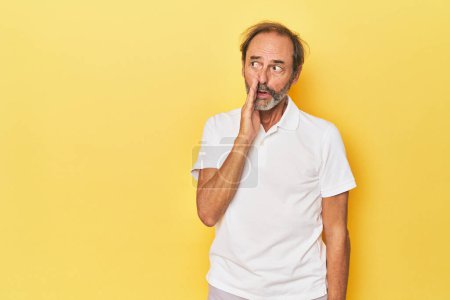 Photo for Caucasian middle-aged man in yellow studio is saying a secret hot braking news and looking aside - Royalty Free Image
