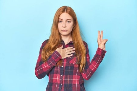 Photo for Redhead young woman on blue background taking an oath, putting hand on chest. - Royalty Free Image