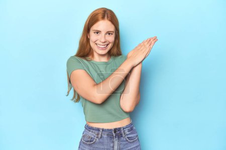 Photo for Redhead young woman on blue background feeling energetic and comfortable, rubbing hands confident. - Royalty Free Image