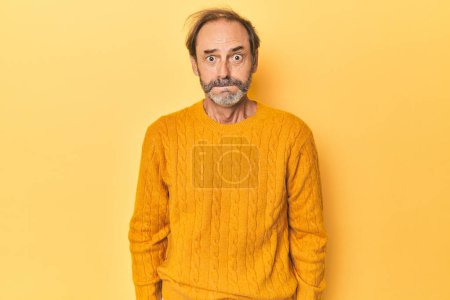 Téléchargez les photos : Homme d'âge moyen caucasien en studio jaune souffle joues, a l'expression fatiguée. Concept d'expression faciale. - en image libre de droit