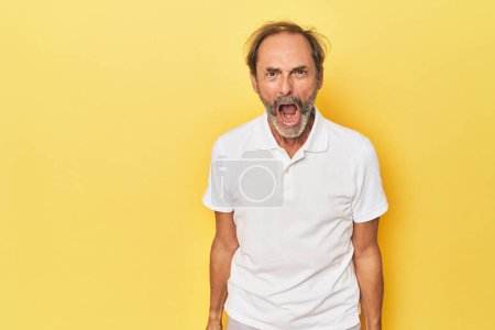 Téléchargez les photos : Homme d'âge moyen caucasien en studio jaune criant très en colère, concept de rage, frustré. - en image libre de droit
