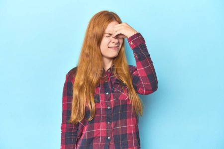 Photo for Redhead young woman on blue background having a head ache, touching front of the face. - Royalty Free Image