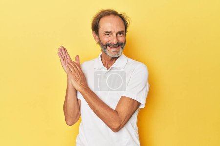 Téléchargez les photos : Homme d'âge moyen caucasien en studio jaune se sentant énergique et confortable, les mains frottées confiantes. - en image libre de droit