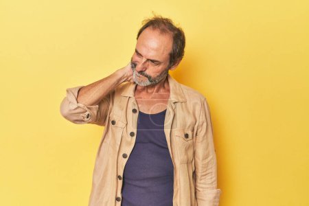 Téléchargez les photos : Homme d'âge moyen caucasien en studio jaune ayant une douleur au cou due au stress, masser et toucher avec la main. - en image libre de droit