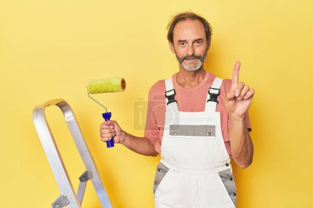 Téléchargez les photos : Homme peinture jaune toile de fond en studio montrant numéro un avec doigt. - en image libre de droit