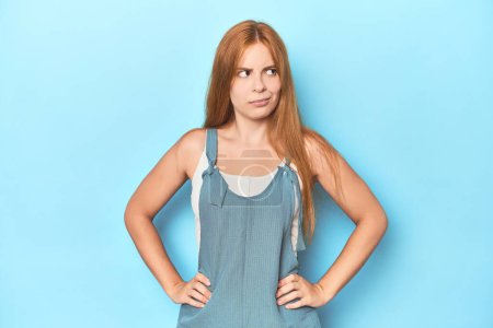 Photo for Redhead young woman on blue background confused, feels doubtful and unsure. - Royalty Free Image