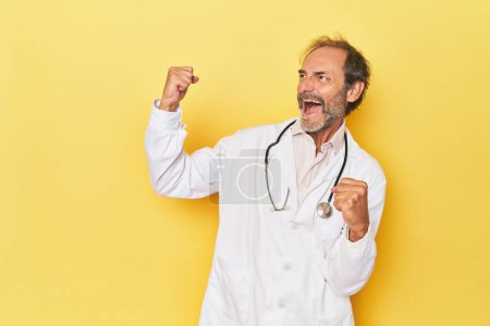 Photo for Doctor with stethoscope in yellow studio raising fist after a victory, winner concept. - Royalty Free Image