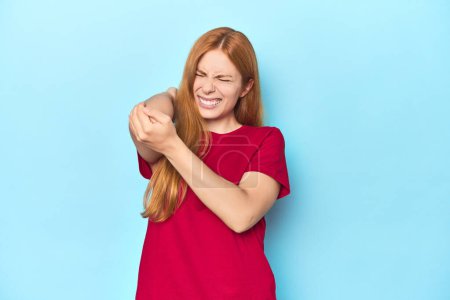 Photo for Redhead young woman on blue background massaging elbow, suffering after a bad movement. - Royalty Free Image