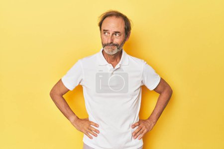 Foto de Caucásico hombre de mediana edad en estudio amarillo confundido, se siente dudoso e inseguro. - Imagen libre de derechos