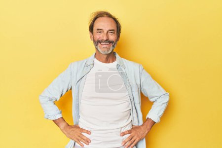 Photo for Caucasian middle-aged man in yellow studio confident keeping hands on hips. - Royalty Free Image