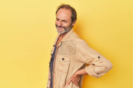 Photo for Caucasian middle-aged man in yellow studio suffering a back pain. - Royalty Free Image