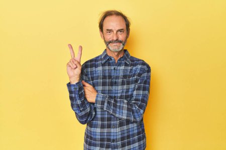 Photo for Caucasian middle-aged man in yellow studio showing number two with fingers. - Royalty Free Image