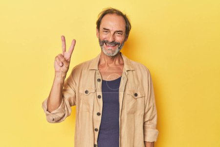 Téléchargez les photos : Blanc homme d'âge moyen en studio jaune joyeux et insouciant montrant un symbole de paix avec les doigts. - en image libre de droit