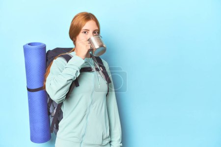 Photo for Mountaineer redhead sipping from camping cup in blue studio - Royalty Free Image