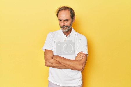 Téléchargez les photos : Blanc homme d'âge moyen en studio jaune fronçant les sourcils face dans le mécontentement, garde les bras croisés. - en image libre de droit