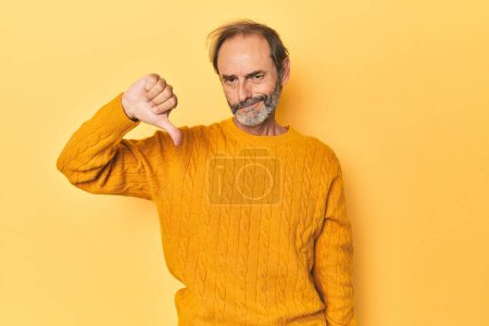 Photo for Caucasian middle-aged man in yellow studio showing thumb down, disappointment concept. - Royalty Free Image