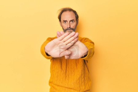 Photo for Caucasian middle-aged man in yellow studio doing a denial gesture - Royalty Free Image