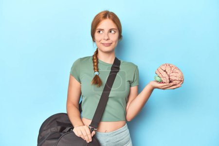 Photo for Sporty redhead with brain model on blue background dreaming of achieving goals and purposes - Royalty Free Image