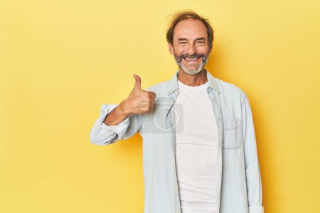 Téléchargez les photos : Blanc homme d'âge moyen en studio jaune souriant et levant le pouce - en image libre de droit