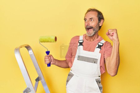 Téléchargez les photos : Homme peinture jaune toile de fond en studio levant le poing après une victoire, concept gagnant. - en image libre de droit