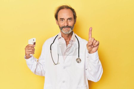Foto de Doctor sosteniendo termómetro infrarrojo en estudio mostrando el número uno con el dedo. - Imagen libre de derechos