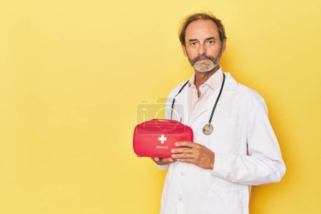 Téléchargez les photos : Médecin avec trousse de premiers soins en studio jaune - en image libre de droit
