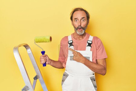 Téléchargez les photos : Homme peinture jaune toile de fond en studio pointant vers le côté - en image libre de droit