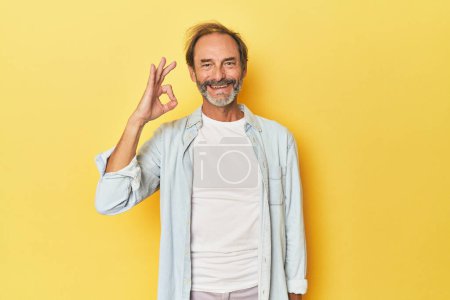 Photo for Caucasian middle-aged man in yellow studio cheerful and confident showing ok gesture. - Royalty Free Image