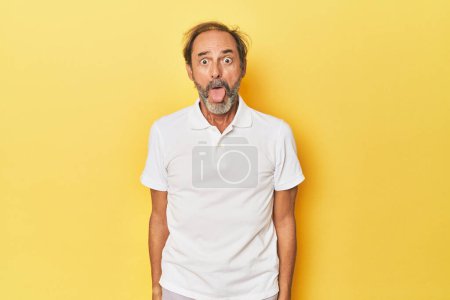 Photo for Caucasian middle-aged man in yellow studio funny and friendly sticking out tongue. - Royalty Free Image
