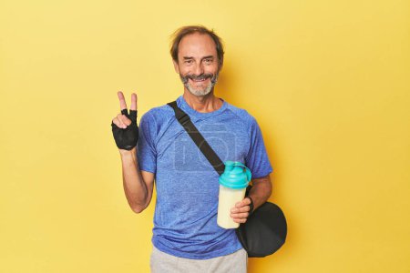 Photo for Gym-goer with protein shake in studio showing number two with fingers. - Royalty Free Image